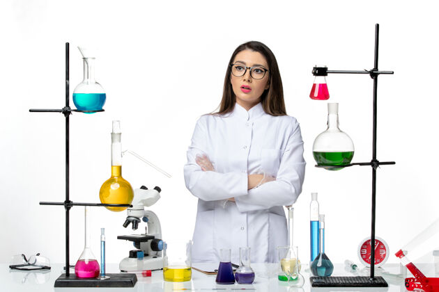 溶液正面图：穿着无菌医疗服的女化学家站在桌子旁 拿着白色背景病毒疾病的解决方案-实验室科学桌子套装视图