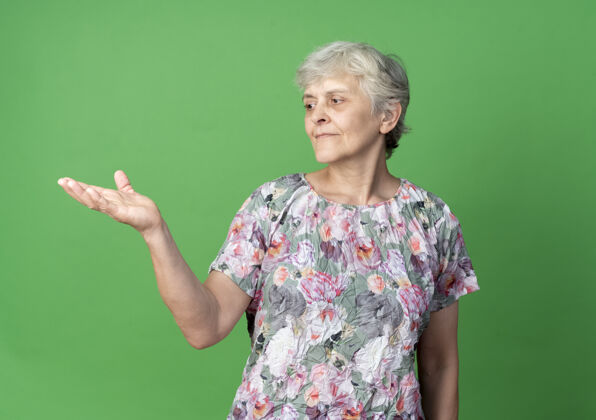 绿的高兴的老妇人看着隔离在绿墙上的空手请空的女人