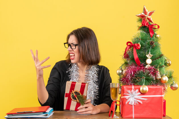 花束一位穿着西装 戴着眼镜 拿着礼物 坐在办公室里一棵圣诞树旁的困惑的商务女士生活人礼物