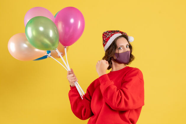 年轻女性正面图年轻女性手持气球 戴着黄色的无菌面具圣诞节乐趣前面
