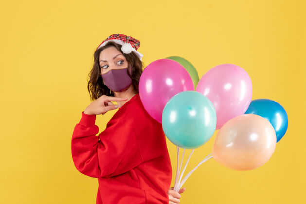 乐趣正面图年轻女性隐藏在无菌面具气球上的黄色背景色节日情感新年圣诞女人情感视图节日