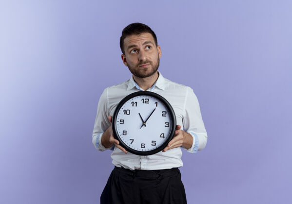 紫色焦急的帅哥拿着钟看着紫色墙上孤立的一面抱着时钟帅气