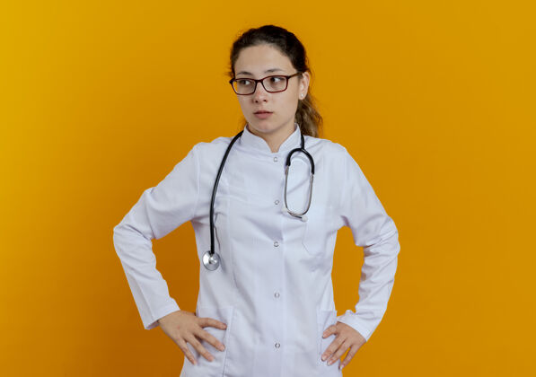 臀部看着身边年轻的女医生穿着医用长袍戴着听诊器戴着眼镜把手放在臀部穿橙色医疗