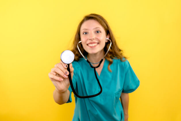 医学黄色墙上女医生使用听诊器的前视图护理女专业