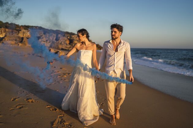 风景一对美丽的情侣在海滩上与蓝色烟雾弹合影的照片情人男性海洋