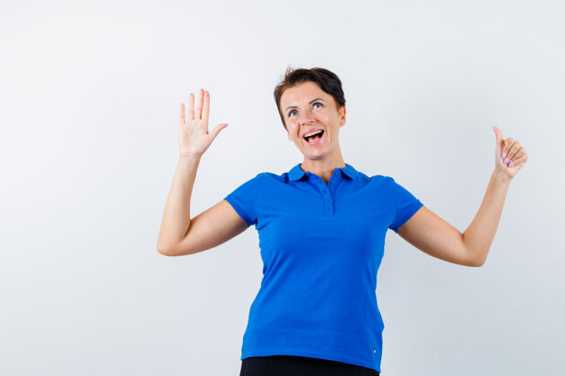 女士成熟的女人在蓝色t恤上展示手掌和拇指向上 看起来很开心 正面视图前面成熟健康