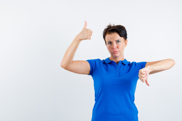 微笑成熟的女人穿着蓝色t恤上下竖起大拇指 看上去犹豫不决 前视图犹豫新鲜护理