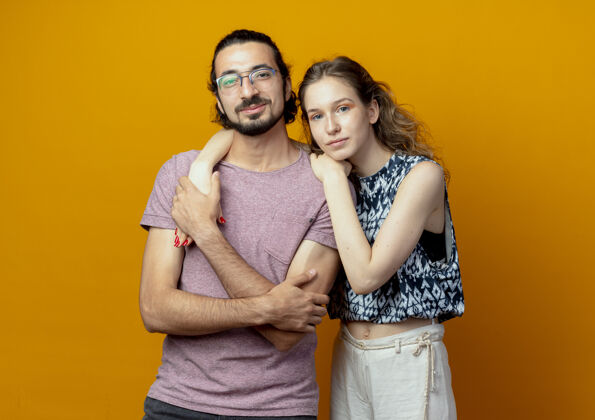 年轻人年轻漂亮的情侣男女在爱情中快乐地看着站在橙色背景上的相机镜头站起来情侣