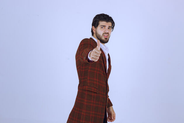 积极一个穿棕色夹克的男人在展示竖起大拇指的招牌工人休闲模特