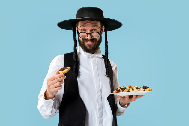 年轻年轻的东正教犹太男子与哈曼塔森饼干节日普瑞姆节日 庆祝 犹太教 糕点 传统 饼干 宗教概念三角形传统种子