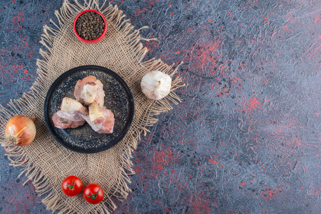 食物在大理石表面放着生鸡肉和蔬菜的黑色盘子生的大腿鸡肉