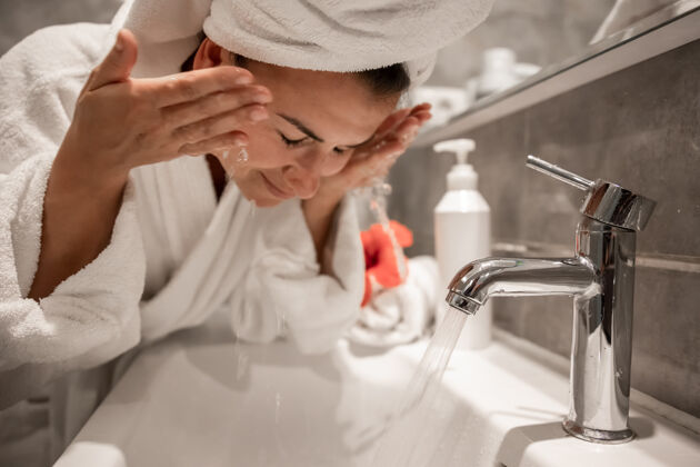 水龙头浴室里的年轻美女头上戴着毛巾 用自来水洗脸卫生洗漱干净