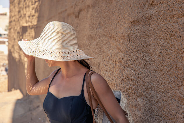 热大热天 一个戴着大草帽的年轻女子躲在沙墙附近躲避阳光女人乡村帽子