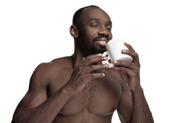 白一个喝着白茶或咖啡的非洲男人 被隔离在白色的工作室背景上一个年轻的裸体快乐的非洲男人的极简风格的特写肖像非洲坐着喝酒