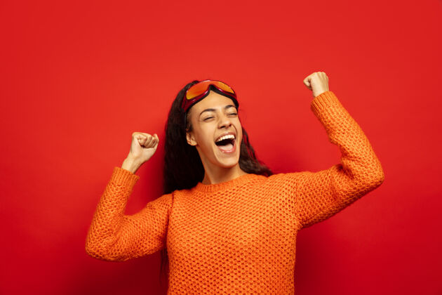 惊喜美国黑人年轻黑发女子的肖像滑雪面具在红色工作室的背景概念的人类情感 面部表情 销售 广告 冬季运动和假日庆祝像赢家表情成人人
