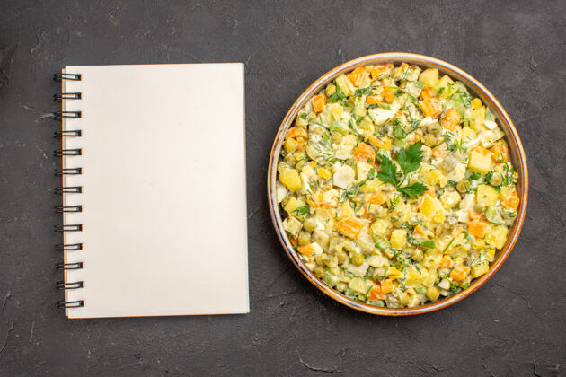 蔬菜在黑暗的表面上用记事本俯瞰美味的沙拉碗晚餐午餐