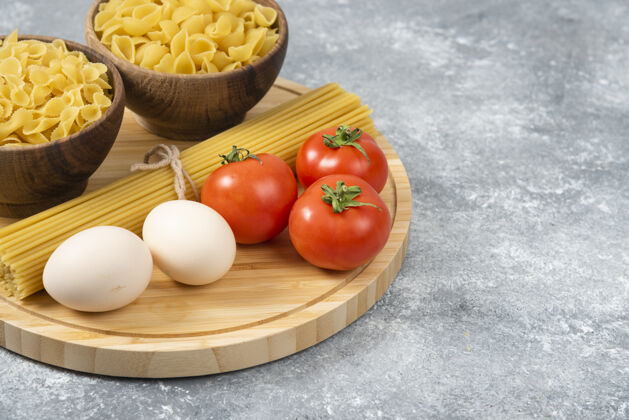 意大利面一碗碗生面食 鸡蛋和新鲜西红柿放在大理石表面通心粉番茄碗