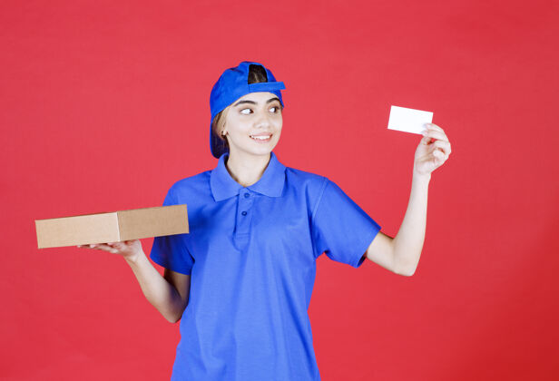 安全穿着蓝色制服的女快递员拿着一个外卖箱 出示她的名片休闲员工模特