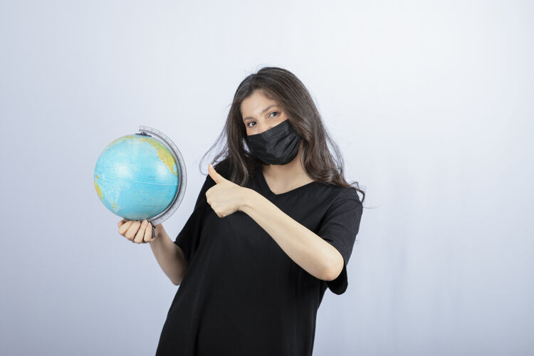 女人戴着医用面具的黑发女人 世界地球仪向上伸出大拇指成人环境人