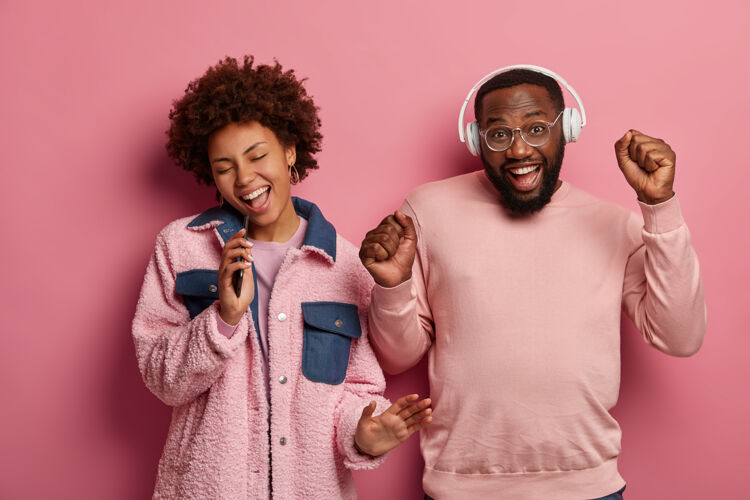 活跃积极的黑皮女人和男人欢欣地与音乐 紧握拳头 在智能手机设备唱歌手机胡须男孩