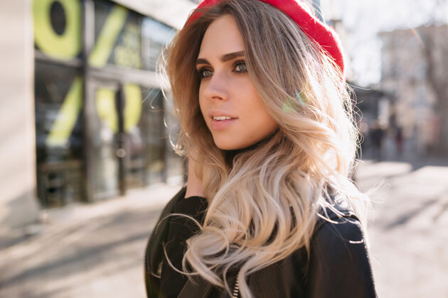 帽子美丽的时尚女孩 金色长发 穿着皮夹克 戴着红帽子 在阳光下 带着快乐的真情走在街上衣服休闲现代