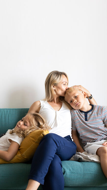 儿子金发妈妈亲吻儿子；我们的头和放松与女儿在沙发上的空白空间女孩关怀亲吻