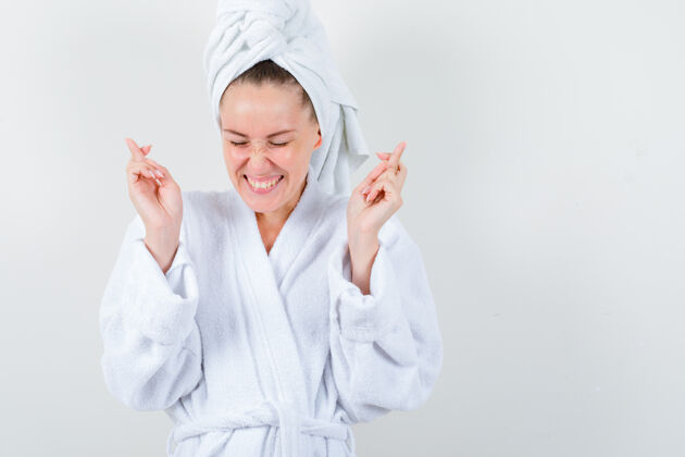 亚洲人年轻的女士在白色浴衣 毛巾和保持手指交叉看起来很高兴 前视图新鲜头发人