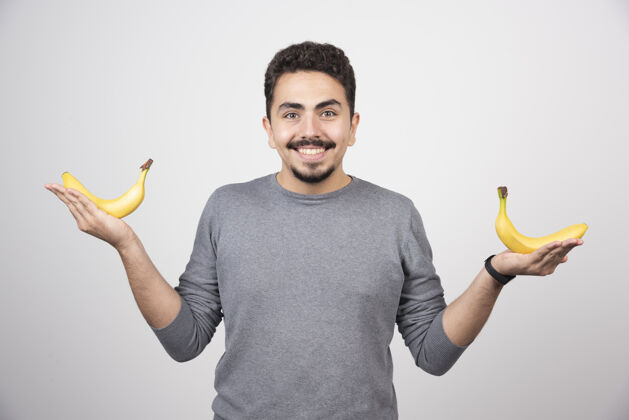 手一个年轻人拿着两个新鲜的香蕉健康食品人指点
