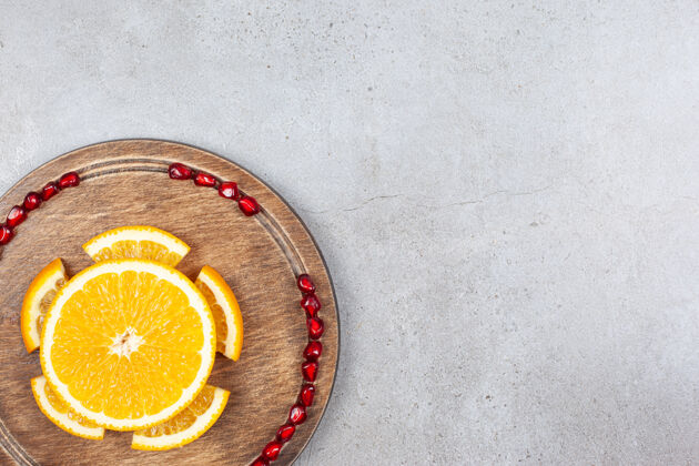 颜色在灰色表面的木板上放着石榴籽的橘子片的俯视图一半成熟特写