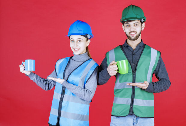 水化男女工程师戴着头盔 拿着蓝色和绿色的杯子刷新工人咖啡