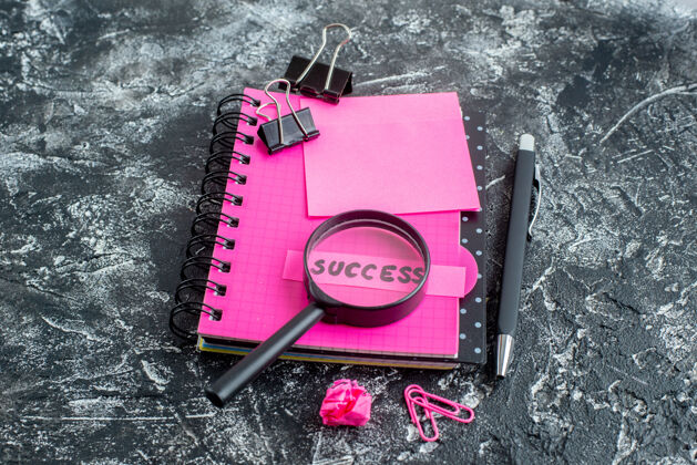 商业前视图粉红色记事本 带笔放大镜和灰色背景上的成功笔记成功大学放大镜