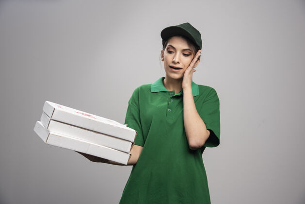 披萨年轻的女信使摆出披萨盒的姿势 捂住耳朵帽子承运人女性