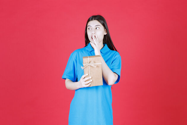 礼物一个穿着蓝色衬衫的女人拿着一个纸板小礼盒 看起来很困惑姿势人生日