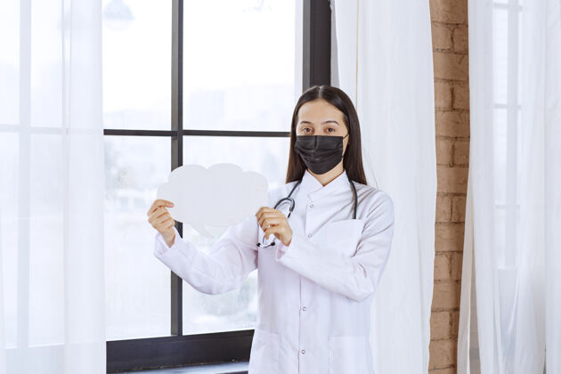 病毒医生拿着听诊器和黑色口罩 手里拿着一块白云形状的智板医疗从业者消毒