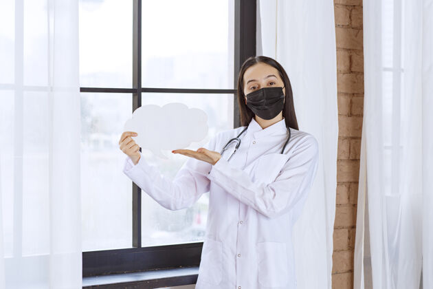 女性医生拿着听诊器和黑色口罩 手里拿着一块白云形状的智板办公桌信息医院