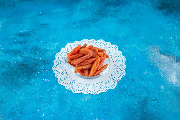 营养把杏干放在蓝色表面的杯垫上的碗里美味天然杏干