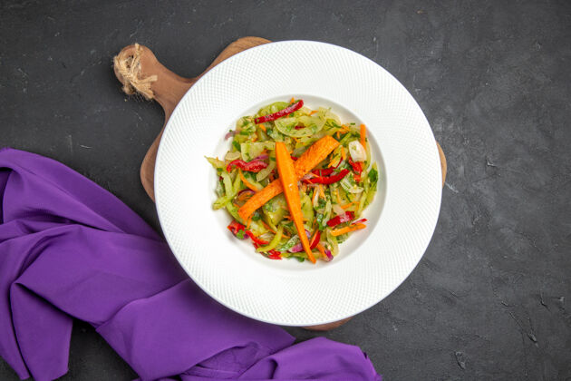 盘子顶部特写查看蔬菜沙拉在切菜板旁边的紫色桌布晚餐桌布胡椒粉