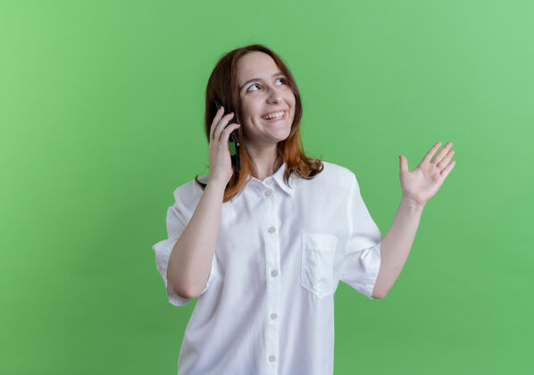 女孩看着一边微笑的年轻红发女孩在电话上说点什么 手放在一边隔离在绿色背景和复印空间手点电话
