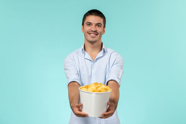 大人正面图：年轻人拿着篮子 手里拿着土豆 微笑着站在蓝色的墙上 孤独而遥远的男性电影院风景男人服务员