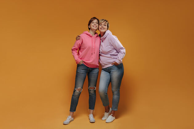 女儿现代的两个女人 一头酷酷的短发 穿着粉色宽边连帽衫 紧身牛仔裤和白色运动鞋 面带微笑地看着镜头牛仔裤衬衫成人