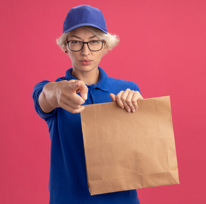 脸身穿蓝色制服 戴着眼镜 拿着纸包 用食指指着粉色墙壁 表情严肃的年轻女送货员严重目录年轻