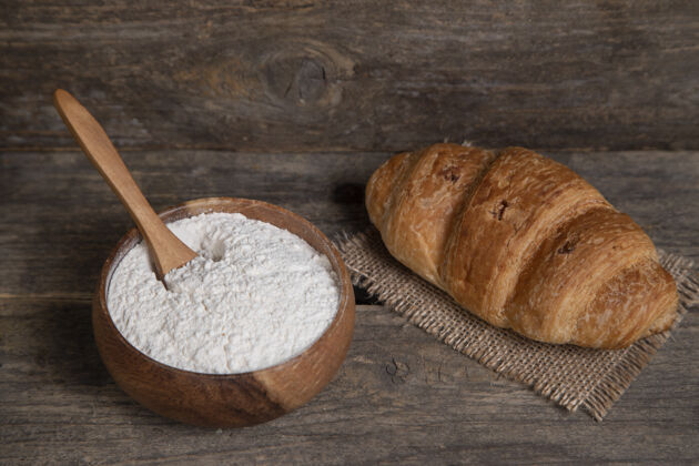 食品一个新鲜的普通牛角面包和一碗面粉木制表面高品质的照片面包法国新鲜