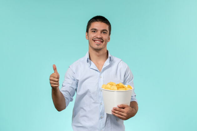 电影正面图：一个年轻人拿着土豆 微笑着站在蓝色的墙上 孤独而遥远的男性电影院电影微笑男人