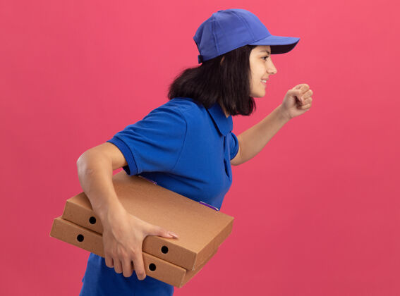 制服一个穿着蓝色制服 戴着帽子的送货员正在粉红色的墙上为顾客运送披萨盒顾客送货披萨