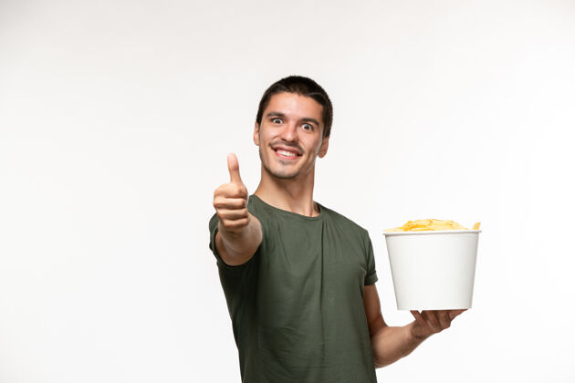 电影正面图身穿绿色t恤的年轻男性手持土豆cips在白墙上像招牌一样展示孤独的电影人喜欢年轻男性土豆