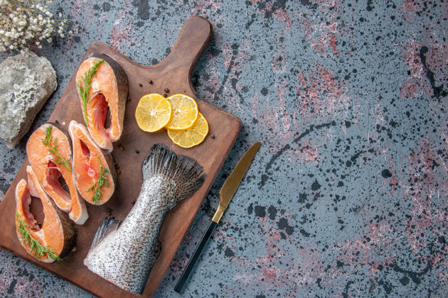 工作新鲜鱼的俯视图柠檬片绿色胡椒在木制砧板上和刀子在蓝黑混色桌上刀胡椒新鲜的鱼