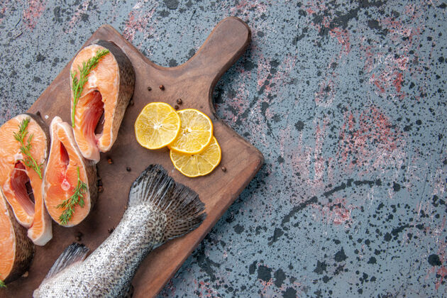 扳手新鲜鱼的俯视图柠檬片青椒放在木砧板上蓝黑混色桌上板木勺食物