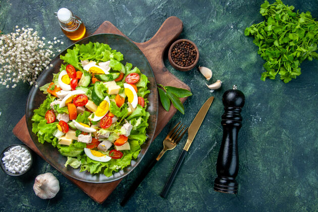 蔬菜上图：美味的沙拉和新鲜的配料放在木质砧板上香料油瓶大蒜素餐具放在黑色的混色桌上食物餐具餐盘