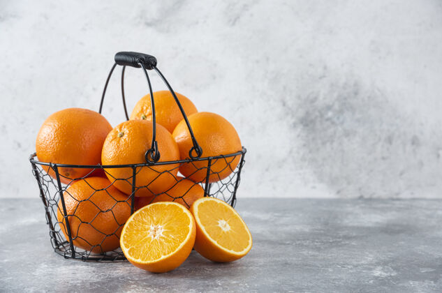 甜点石桌上放着一个装满多汁橙子的金属黑色篮子圆形橙子天然