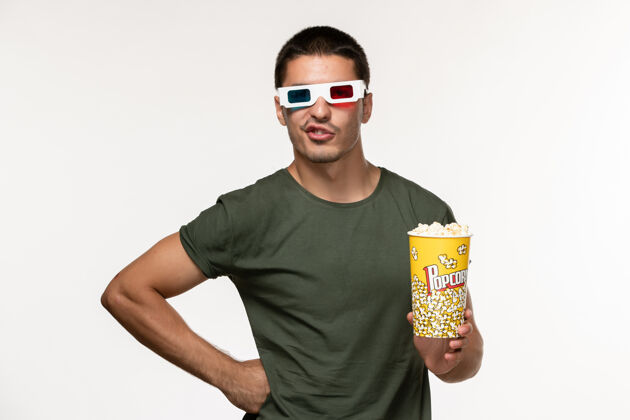 电影正面图身着绿色t恤的年轻男性手持爆米花包戴着d墨镜在白墙上拍摄电影孤独电影院男性电影电影院肖像电影